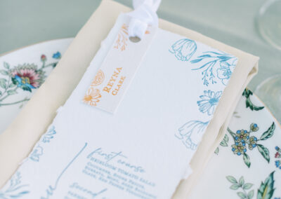 Wedding menu and name card with floral design placed on a floral-patterned plate and beige napkin.