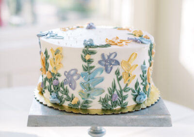 A round cake on a stand, decorated with colorful floral designs in icing.