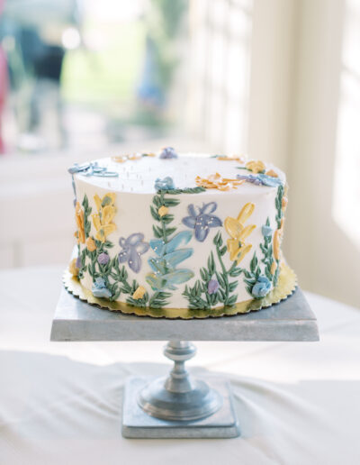 A round cake on a stand, decorated with colorful floral designs in icing.