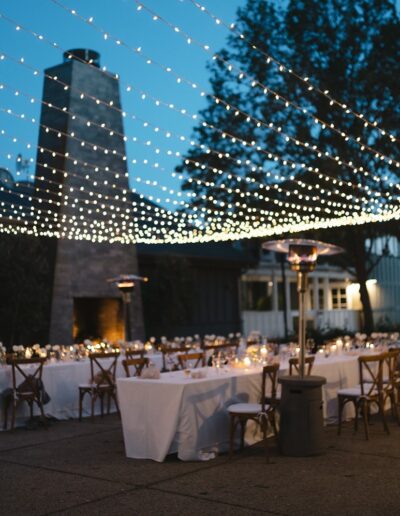 Outdoor evening wedding reception with tables and chairs arranged under string lights.