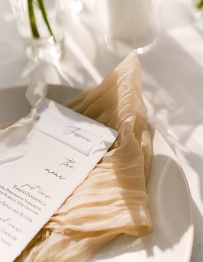 A beige napkin and menu set on a white plate with sunlight casting shadows.