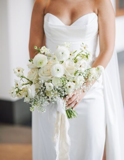 Bride in a white dress holding a bouquet of white flowers with hints of greenery.