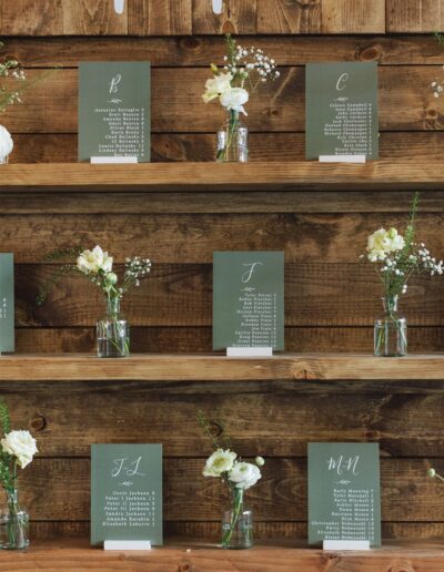 Wooden shelves displaying floral arrangements and seating cards with letters and names.