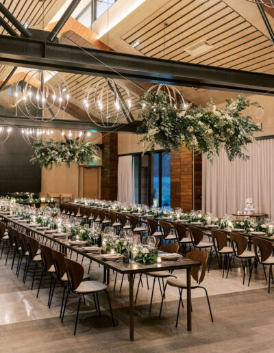 Elegant dining hall with long tables set for an event, featuring hanging greenery and modern spherical chandeliers.