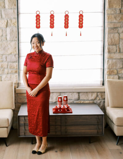 A woman in a red dress stands in a room with stone walls and Chinese decorations in the background.