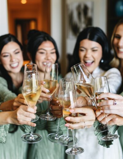 Five people clink champagne glasses in a celebratory toast, smiling and standing close together indoors.