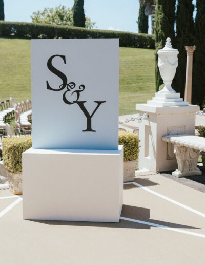 Outdoor setup with chairs and greenery for an event. A large display with "S & Y" is in the foreground.