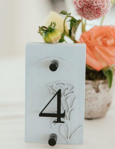 Table number four sign with floral cutout, set beside a small flower arrangement in a pot, including roses and other blooms.