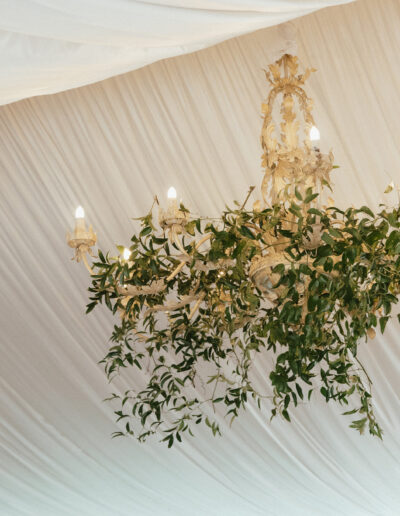 An ornate chandelier decorated with greenery hangs from a white draped ceiling.