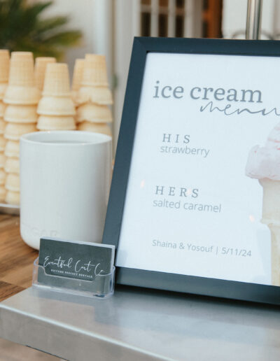 A table displays a framed ice cream menu listing flavors, stacked cones, a mug, and a business card holder.