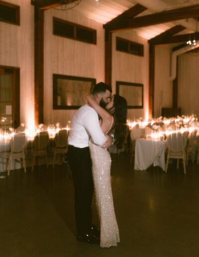 A couple embraces and kisses on a dimly lit dance floor in an elegant room with wooden walls and ambient lighting.