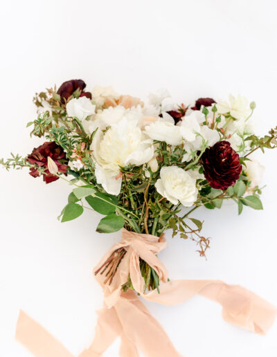 Bouquet of white and dark red flowers with green foliage, tied with a pink ribbon on a white background.