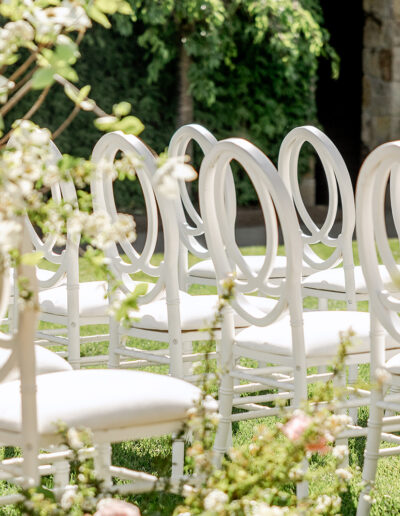 Rows of white chairs with looped backs arranged on green grass amid white floral arrangements.