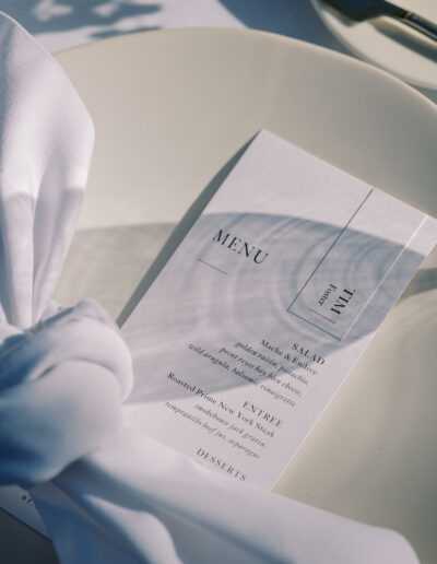 A white dinner plate with a neatly folded white napkin and a printed menu card listing salad, entrée, and dessert options.