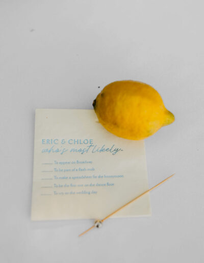 A lemon, a toothpick, and a card with "Eric & Chloe what’s most likely" and a checklist with various options are on a white surface.