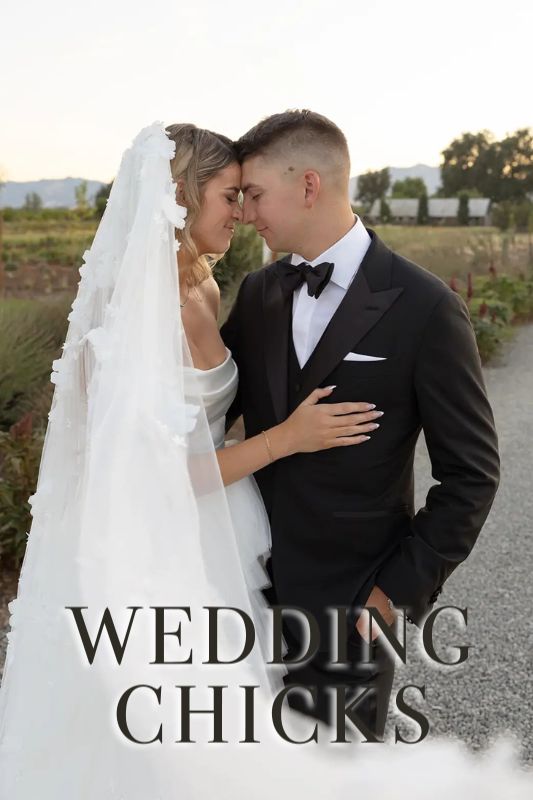 A bride and groom stand close together outdoors, touching foreheads; the bride wears a white gown and veil, the groom wears a black tuxedo. Text reads "WEDDING CHICKS.