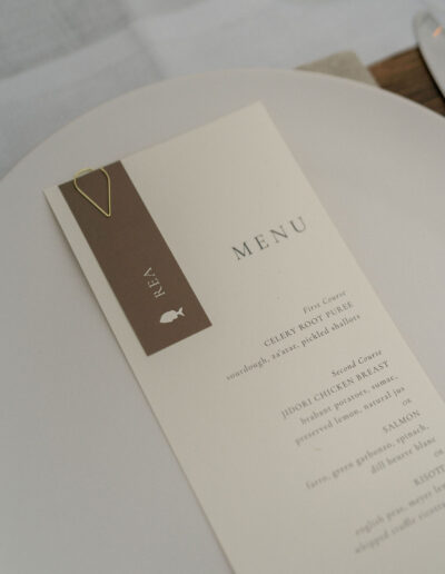 A beige and brown restaurant menu with a gold paperclip rests on a white plate, listing courses including chicken and salmon.
