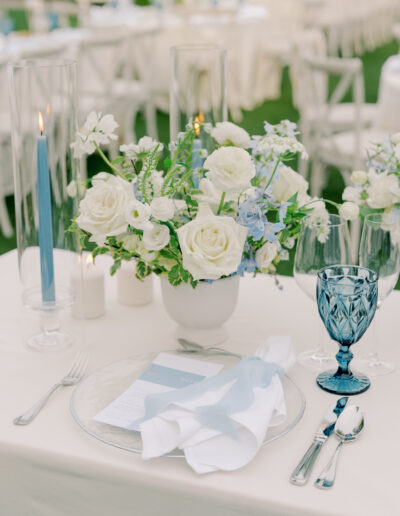 Elegant table setting at a Solage Calistoga wedding with a white and blue floral centerpiece, blue candle, blue glass goblet, white napkin, and menu on a clear plate.
