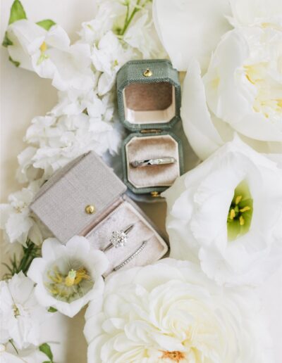 Two vintage-style rings in velvet boxes are displayed among white flowers, including roses and lisianthus.