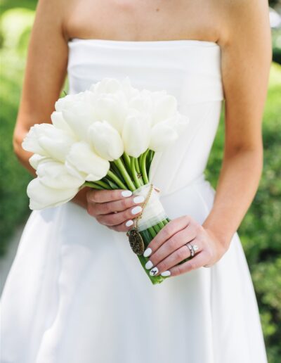 A person in a white strapless dress holds a bouquet of white tulips, displaying a ring and white manicured nails.