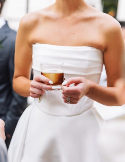A woman in a strapless white dress holds a cocktail glass with a foamy drink.